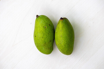 Two fresh green raw mango on a wooden background