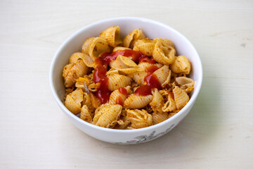 Delicious shell pasta with tomato sauce in a white bowl on wooden background. 