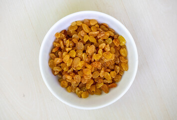 Delicious raisins in a white bowl on wooden background. Raisins are dried grapes.​ Its scientific name is Vitis vinifera. In the Bengali language, it is called Kismis or Kishmish. Top view