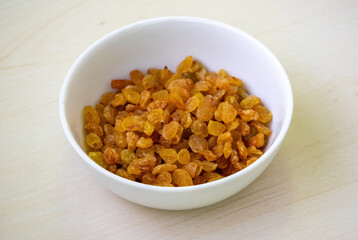 Delicious raisins (Vitis vinifera) in a white bowl on wooden background.  