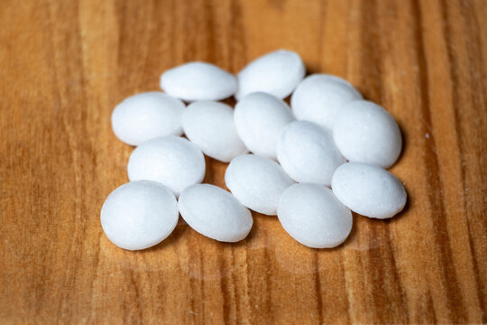 Naphthalene balls isolated on wooden background. It is also known as moth balls, naphthalin, moth flakes, antimite, and hexalene.