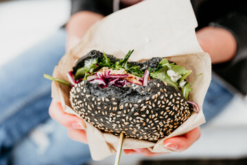 Close up of woman hands holding delicious organic salmon vegetarian burger on open air beer an...