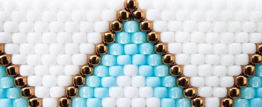 Macro shot of boho style beading backdrop. White, blue and bronze color beading pattern.