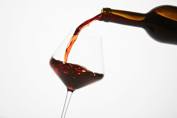 Red wine pouring into tilted wineglass from bottle. - 795240094