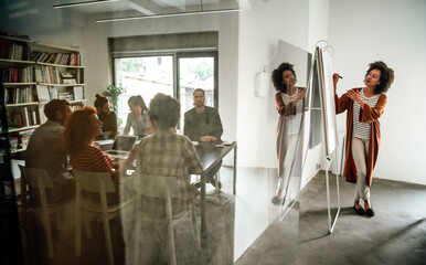 Young businesswoman leading a discussion during a meeting with her colleagues. - obrazy, fototapety, plakaty