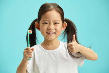 Sweet chinese child kidl wearing in white t shirt use toothbrush, showing thumb up gesture, stands over blue isolated background with a free copy space. Children oral hygiene concept. - 795252862