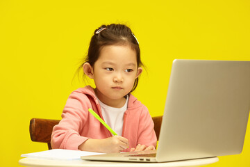 Studio portrait of Concentrated Asian Child in Distance Learning Session over isolated yellow. Young korean pupil Engages in Remote Study
