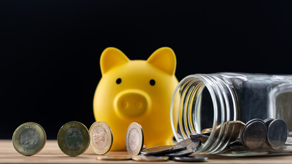 Coins rolling out of a fallen jar with a yellow piggy bank behind - finance and investment concept.