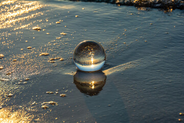 Glass ball lies in the water in the waves at the sea