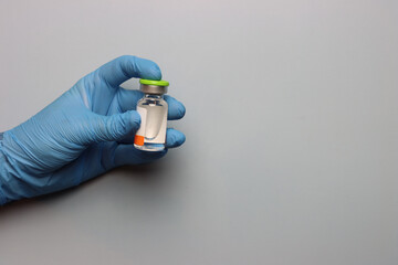 Drug vial in the left side been hold by a person wearing glove with a copy space in the right. 