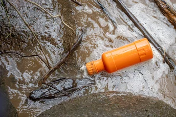 Deurstickers selective focus orange chemical bottle in the river Throwing the garbage without considering nature A bottle of insecticide, the garbage of a careless farmer. There is space for text. © Core