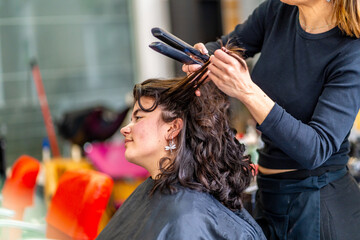 Woman sitting in hair salon while hairstylist ironing the hair