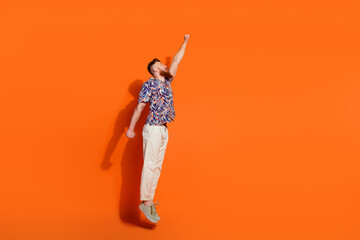 Full length photo of attractive guy wear print shirt white trousers raising fist up fly to empty...