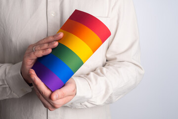 Rainbow flag from paper in man hands in white t-shirt. LGBT flag. LGBTQIA Pride Month in June....