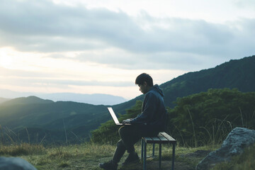 East Asian remote worker finds a serene spot outdoors to set up their mobile office.