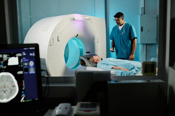 Selective focus shot of mature Caucasian woman having CT scan procedure in modern clinic, biracial doctor working with her - Powered by Adobe