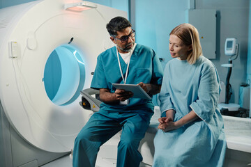 Mature biracial radiographer showing X-ray image on digital tablet to mature Caucasian female patient after CT procedure, copy space - Powered by Adobe