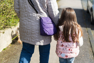 Back view of a Grandmother and daughter walking in the street together.