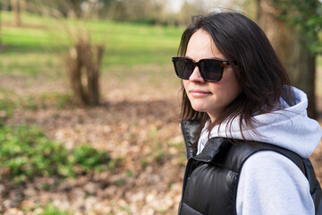 Young woman in black coat and sunglasses standing in the park and looking away