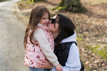 Mother kissing her daughter on the cheek in a park in springtime