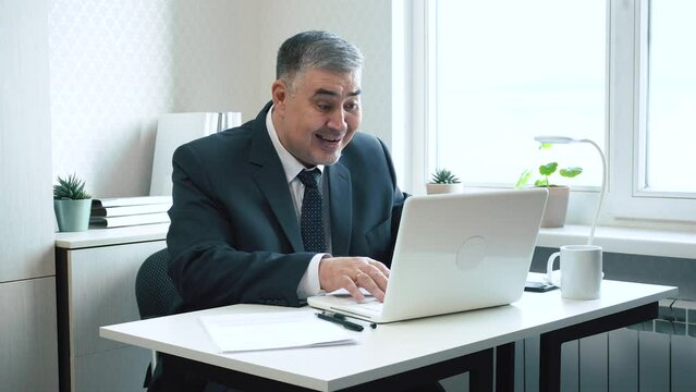 A businessman in the office ecstatically shouts while looking at the computer screen. Ideal for content on making right decisions, successful investments, and lucrative contracts.