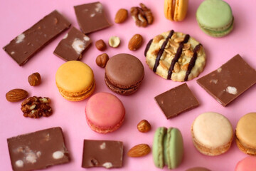 Pastel macarons, almond chocolate, peanut butter cookies and various nuts on bright pink background. Selective focus.