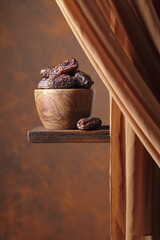 Dried medjool dates in wooden dish on a brown background.