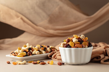The mix of various nuts and raisins in a white bowl on a beige background.