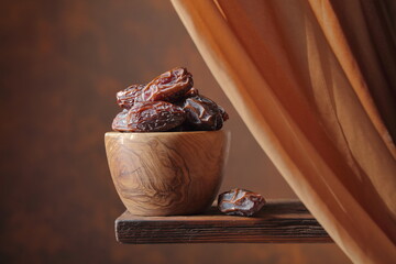 Dried medjool dates in wooden dish on a brown background.