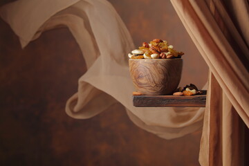 Mix of various nuts and raisins in a wooden bowl on a brown background.