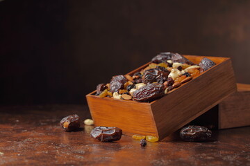 Dates, nuts, and raisins in a wooden box on a brown background.