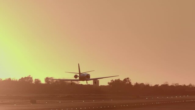 Small private jet approaches for landing against a sunset sky, with runway lights visible