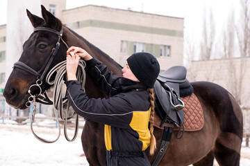 Person adjusting reins on saddled horse outdoors.