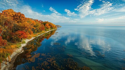 A scenic overlook of a vast and wide freshwater lake, with colorful autumn foliage lining the shoreline and reflecting in the calm waters below. - obrazy, fototapety, plakaty