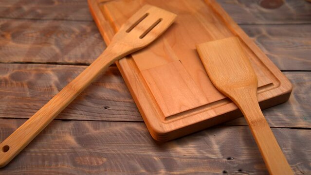A wooden cutting board is shown with a spatula resting on top of it. The spatula is positioned in the center of the board, creating a simple yet functional kitchen setup.