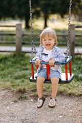 little child on swing, a small child with blond hair sits on a swing. 
