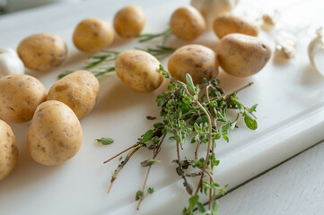 Fresh and raw potatoes on a white cutting board with herbs