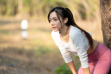 Young female runner with hands on hips standing on a path in a park, taking a break from training.