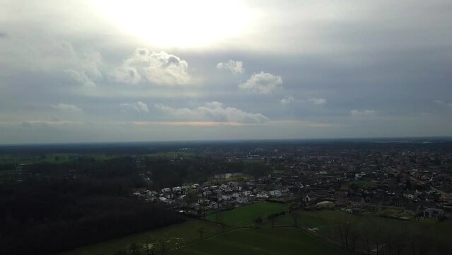 This footage presents an aerial perspective of a suburban landscape under a sprawling overcast sky. The expansive view reveals the town's layout, with residential areas interspersed with green spaces