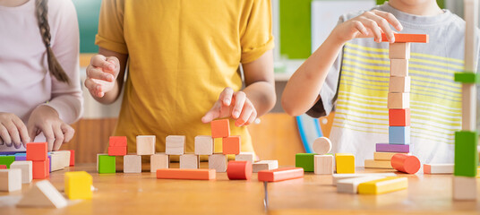 close up hands of little children playing blocks in classroom. Learning by playing education group study concept. International pupils do activities brain training in primary school background banner