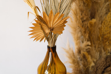 A tasteful arrangement of fluffy pampas grass stalks elegantly placed within an amber glass vase,...