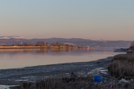 visuale dettagliata, dalla foce del fiume Isonzo sul mare Adriatico, di parte della costiera triestina e delle colline e delle montagne slovene, sotto un cielo sereno, al tramonto