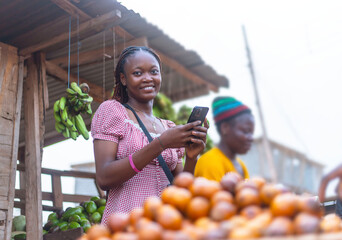 Smiling African Saleswoman Using Mobile Phone at Fruit Stand
