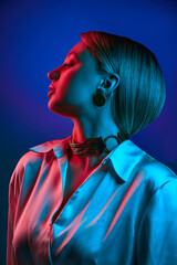 Aesthetic expression of current fashion, presenting minimalist makeup with striking jewelry. Model posing against blue background in neon light. Concept of modern fashion, trendy style, beauty, youth