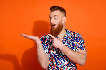 Photo of cheerful impressed guy dressed print shirt looking showing arm pointing finger emtpy space...