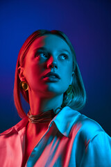Chic modern style. Elegant young woman wearing sarin shirt and golden luxurious jewelry against blue background in neon light. Concept of modern fashion, trendy style, beauty, youth culture