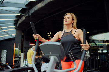 Mature woman exercising on training machine in modern health club for retirements. Woman staying healthy with exercise. Concept of sport, active seniors in modern life, healthy lifestyle. Ad