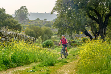 active senior woman cycling with her electric mountain bike in the rough landscape of National Parc Serra de São Mamede near Marvao in central Portugal, Europe - 795370257