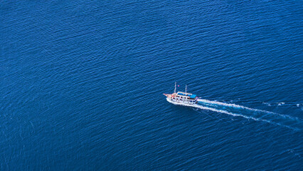 AERIAL: A boat creates a white wake while sailing across the endless blue sea. - obrazy, fototapety, plakaty