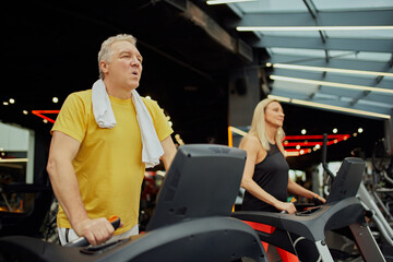 Senior fitness enthusiasts engaged in treadmill session at modern fitness center. Active older...